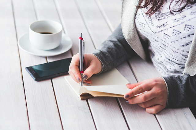 une femme qui ecrit sur son carnet devant une tasse de cafe